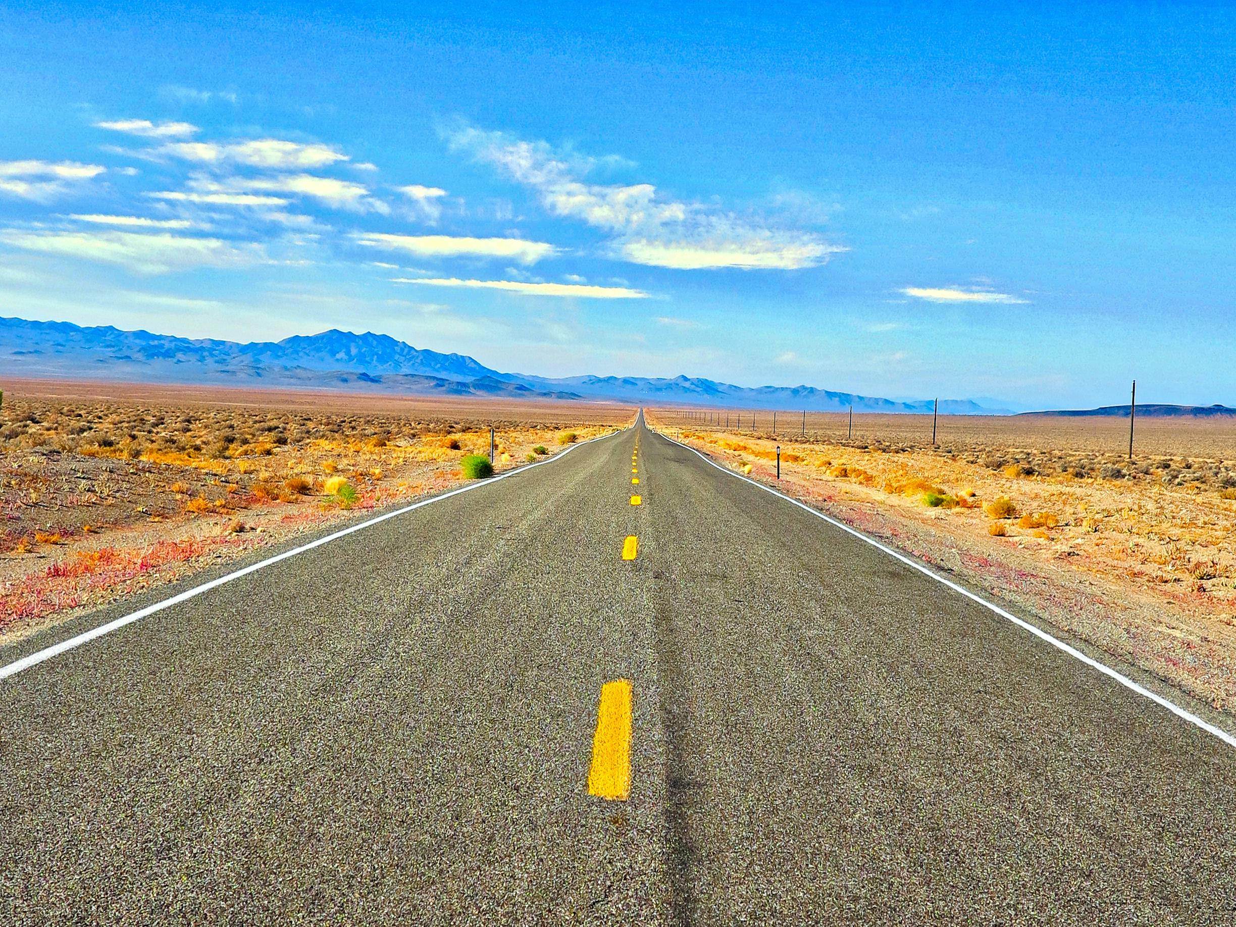 A long straight road in the Nevada desert under a blue sky, perfect for travel and adventure.